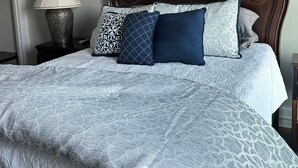 Quarto com cama grande, mesa de cabeceira, abajur e parede com textura.