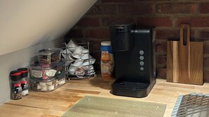 Uma cozinha com cafeteira, prateleiras com louças e uma parede de tijolos.