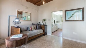 A spacious living area with a wooden ceiling, a grey sofa with patterned cushions, a round wooden table, and a kitchen visible through an open doorway. - Canal Place: Boat Dock, Pool & Spa, On Canal by Anna Maria Life Vacation Rentals (Anna Maria)