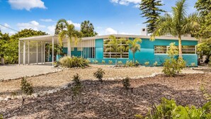 A two-story building with a light blue exterior, numbered 238, featuring a covered patio area with a lattice fence and various tropical plants. - Canal Place: Boat Dock, Pool & Spa, On Canal by Anna Maria Life Vacation Rentals (Anna Maria)