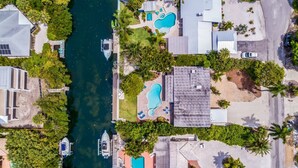 An aerial view of a coastal residential area with multiple swimming pools, a marina with boats, and lush greenery. - Canal Place: Boat Dock, Pool & Spa, On Canal by Anna Maria Life Vacation Rentals (Anna Maria)