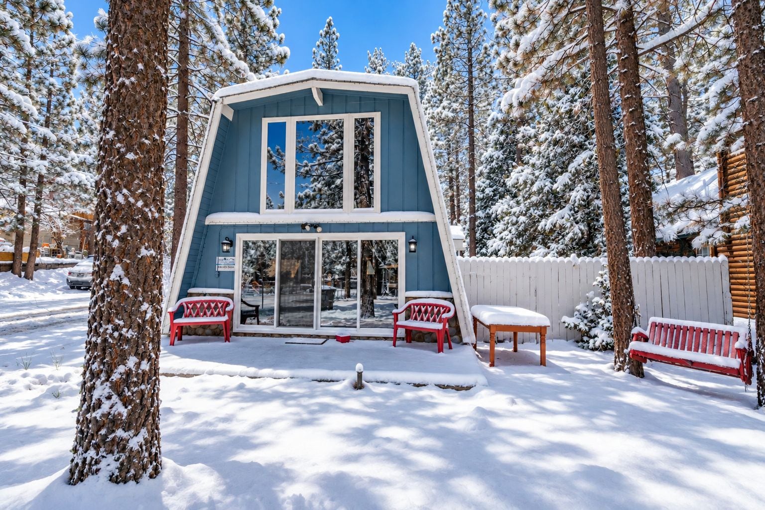 A two-story cabin with a glass door entrance, surrounded by snow-covered trees.