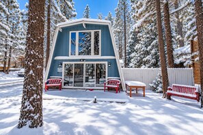 A two-story cabin with a glass door entrance, surrounded by snow-covered trees. - Sherwood Pines (Big Bear City)