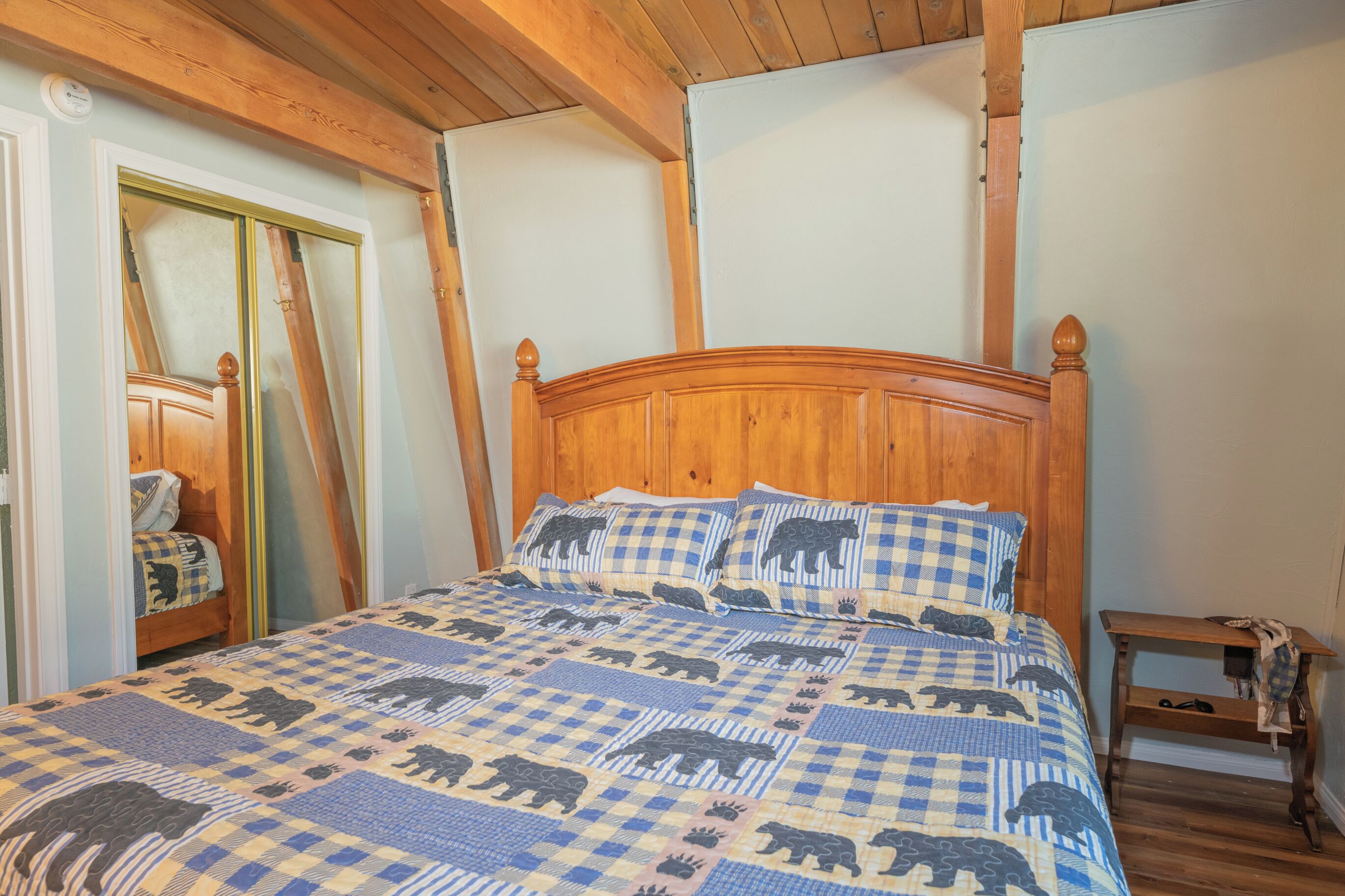 A bedroom with a wooden bed, checkered bedding, a wooden nightstand, and a mirror.