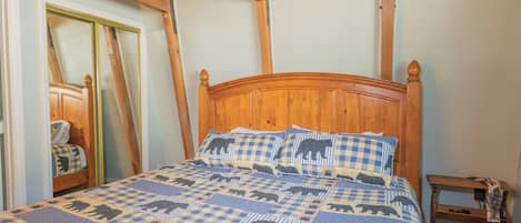 A bedroom with a wooden bed, checkered bedding, a wooden nightstand, and a mirror.