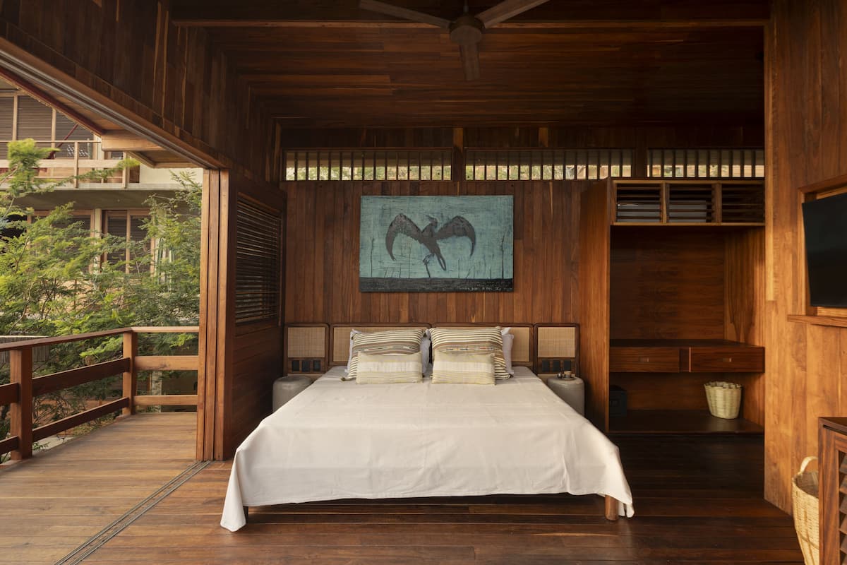 Un dormitorio de madera con una cama, cabecera de madera y un ventanal grande.