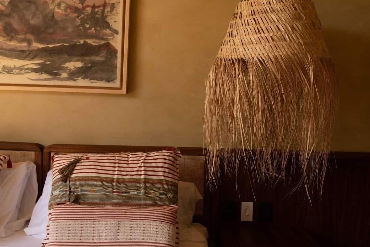 Una cama con almohadones a rayas y una lámpara colgante de fibras naturales.