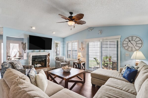 A living room with a fireplace, a ceiling fan, and a large clock on the wall.