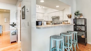 Une cuisine moderne avec des meubles blancs, un îlot central et des tabourets de bar bleus.