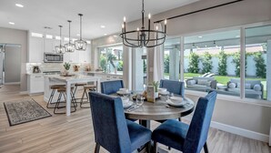 A modern kitchen with white cabinets, a central island, and a dining area with blue chairs and a round table. - Paradise Villa - Spacious Home with Private Pool, Office, and Pool Table in Scottsdale (Scottsdale)