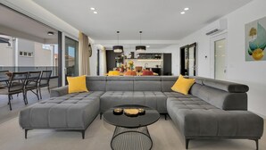 A modern living room with a grey sectional sofa, a round coffee table, and a dining area with chairs and a table.
