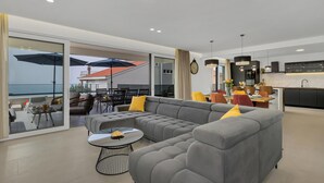 A modern living room with a grey sectional sofa, a small round coffee table, and a dining area with a table and chairs.