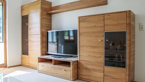 A modern living room with a flat-screen TV, wooden cabinets, and a glass coffee table. - Ferienwohnung - Wald am Arlb. (Wald am Arlberg)