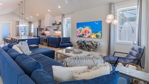 En moderne stue med en stor blå sofa, et spisebord og et køkken i baggrunden.