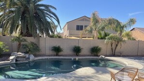 A swimming pool with a curved edge, surrounded by a low stone wall, palm trees, and a house in the background. - Chandler retreat, golfers home away from home. STR license309317
tpt21606535 (Chandler)