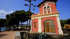 A red and white building with a clock tower, surrounded by trees and a beach view.