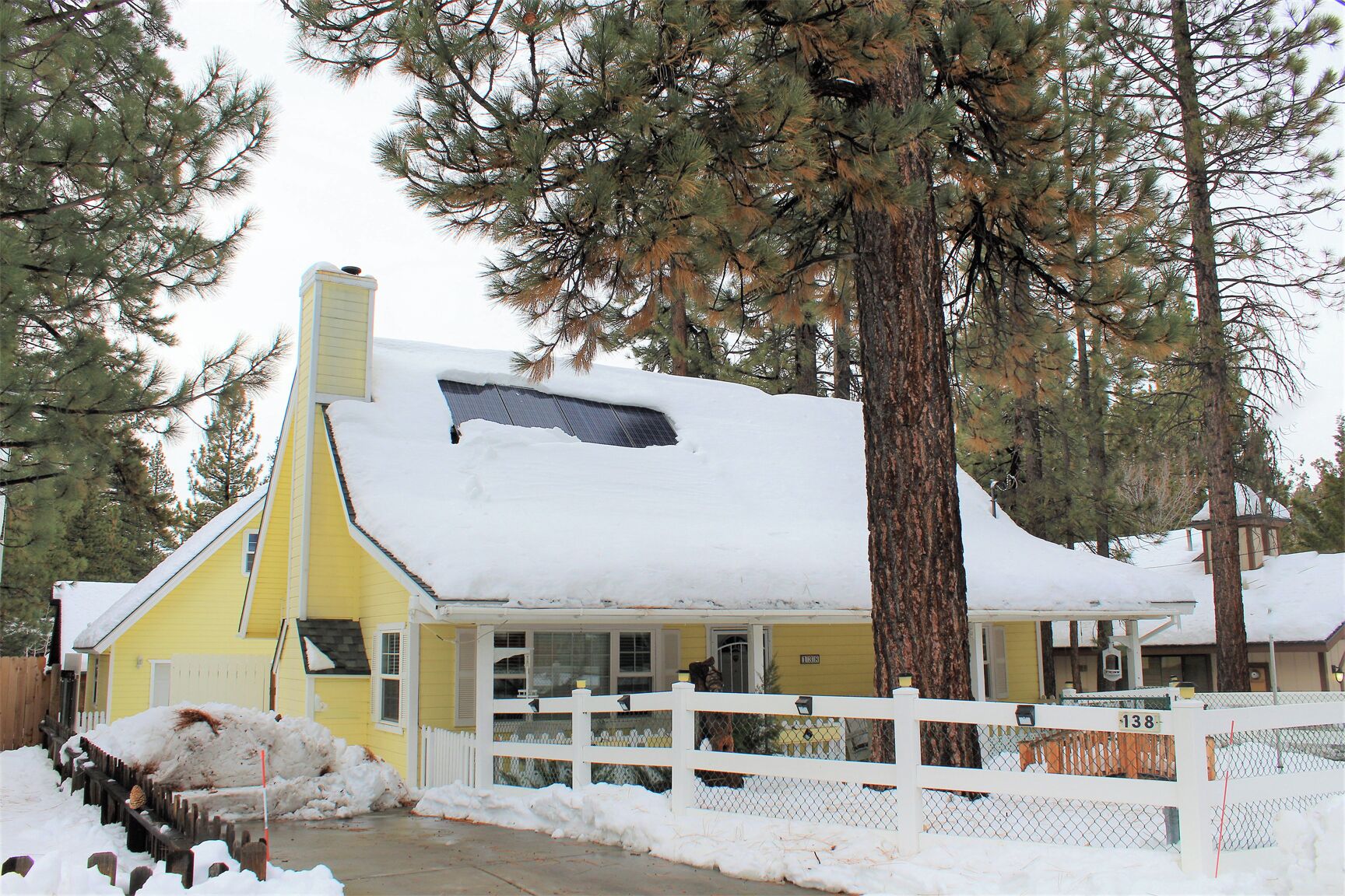 Una casa amarilla con cerca blanca, rodeada de nieve y árboles.