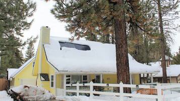 A yellow house with a white fence, surrounded by snow and trees.