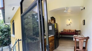 A compact living space with a sliding glass door leading to a balcony, a kitchenette with a refrigerator, a wooden dining table, and a sofa. - Enchanted Monkey Apartment  (Quepos)