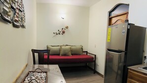 A compact living space with a sofa, a dining table with a basket of seashells, a refrigerator, and a wooden cabinet. - Enchanted Monkey Apartment  (Quepos)
