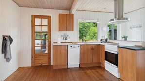 A modern kitchen with wooden cabinets, a dishwasher, an oven, and a window with a view of greenery. - 3 bedroom beautiful home in Ebeltoft (Ebeltoft)