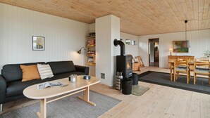 A cozy living room with a black sofa, a wooden coffee table, a fireplace, and a dining area with wooden chairs and a table. - 3 bedroom beautiful home in Ebeltoft (Ebeltoft)