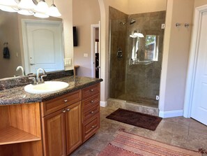 Une salle de bain avec un lavabo sur un plan de travail en granit, des meubles en bois, une cabine de douche en verre et un tapis à motifs.