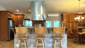 Una cocina con armarios de madera, un refrigerador de acero inoxidable, una isla central con tres taburetes de madera y una campana extractora moderna de acero inoxidable.