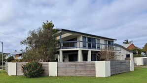 Uma casa moderna de dois andares com varanda, cercada por um gramado bem cuidado e cerca de madeira.