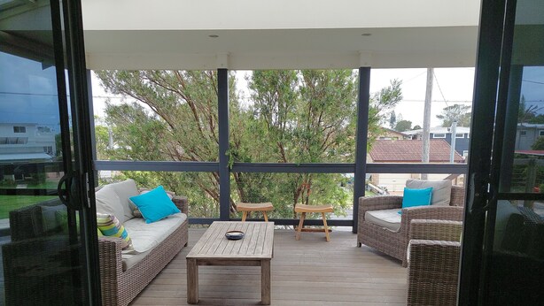 Pátio externo com móveis de vime, uma mesa de madeira e vista para árvores e casas.