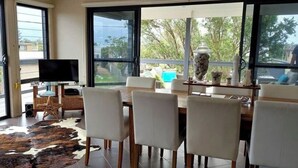 Uma sala de jantar com uma mesa grande e cadeiras, uma televisão em um suporte e vista para o verde lá fora.