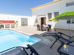 A poolside area with a pool, lounge chairs, a table with chairs, and a green umbrella. - House with swimming pool, wifi and barbecue (Dúrcal)