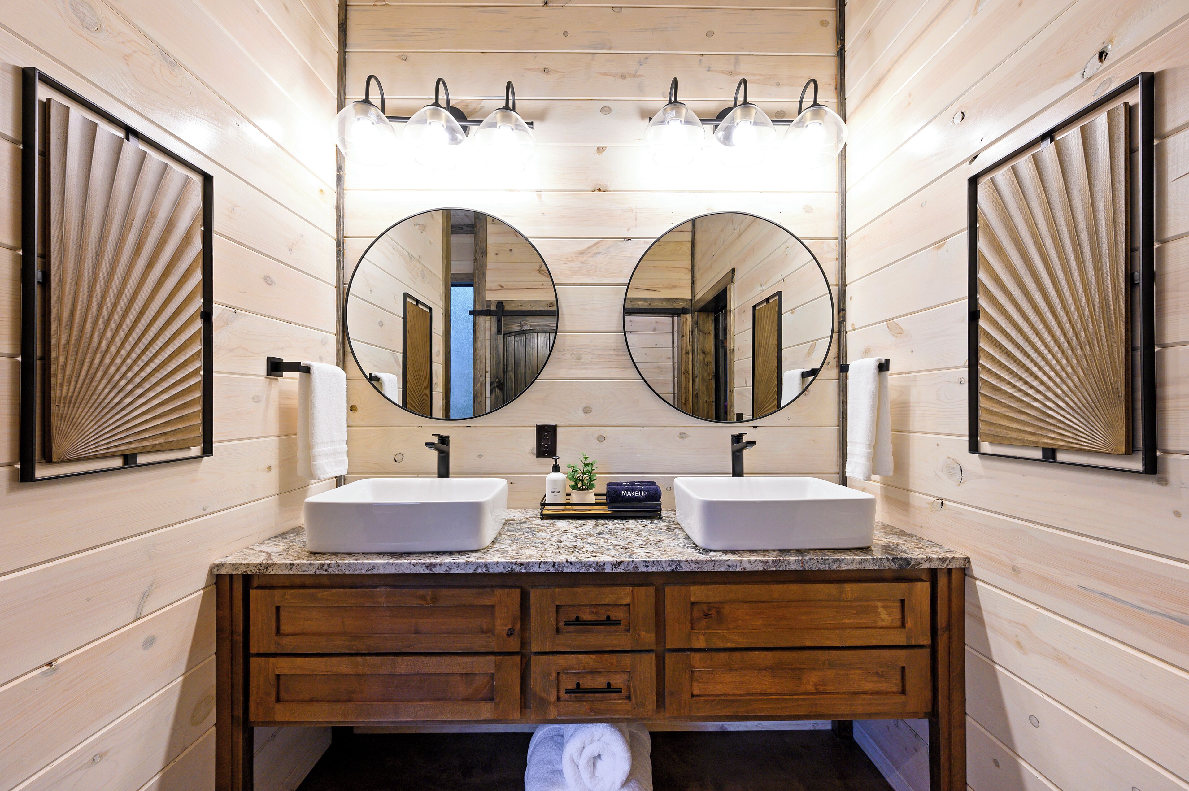 Une salle de bain avec des lambris en bois, deux lavabos, un meuble-lavabo avec des tiroirs et de grands miroirs.