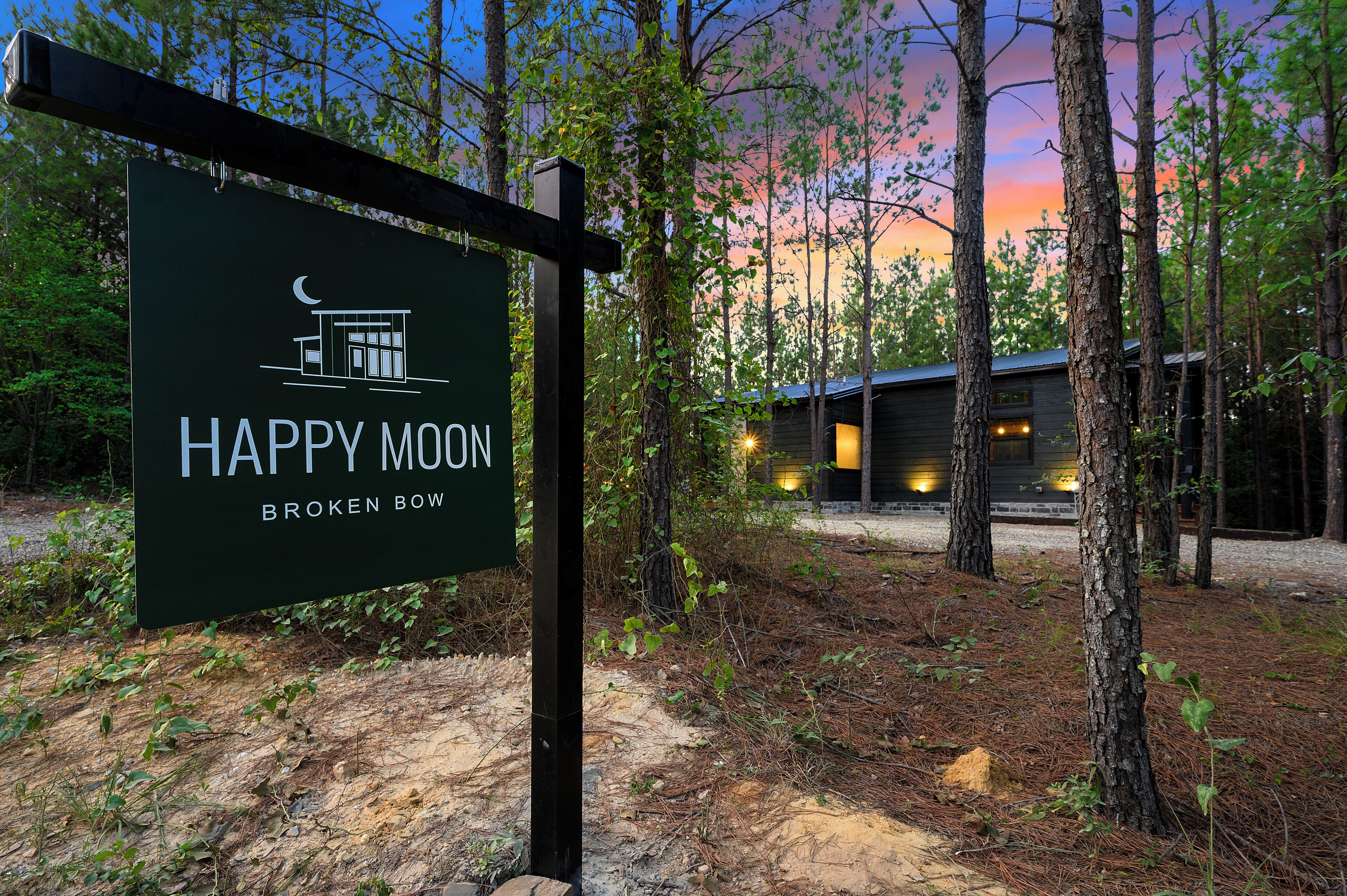 Une enseigne indiquant « Happy Moon Broken Bow », avec une cabane en arrière-plan.