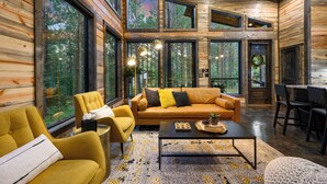 Un interior de cabaña de troncos moderno con un sofá grande, sillones amarillos y un comedor.