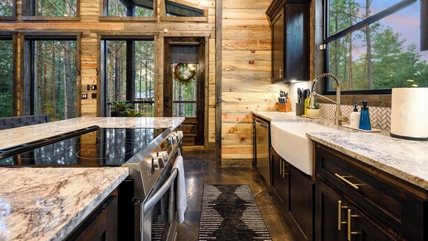 Una cocina moderna con una isla grande, horno empotrado y vistas al bosque a través de amplias ventanas.