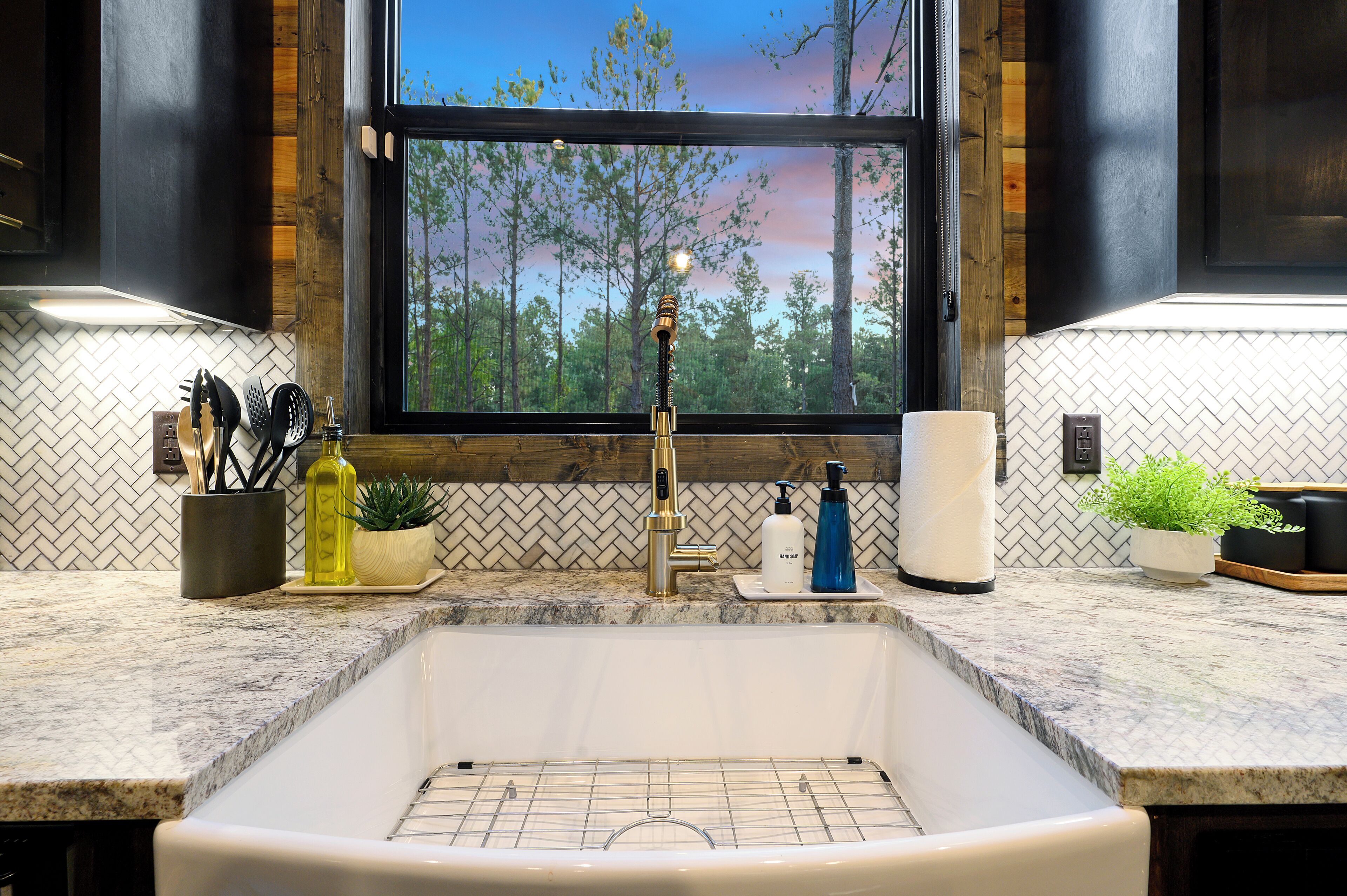 A kitchen with a large window, a sink, and various kitchen items on the counter.