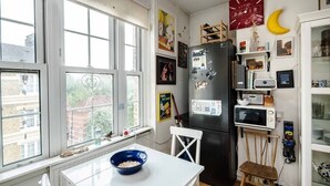 Eine Küche mit einem weißen Tisch, einem schwarzen Kühlschrank und einem Fenster mit Blick auf Gebäude.