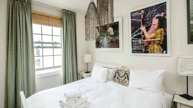 Ein Hotelzimmer mit einem großen Bett, einem Fenster mit Vorhängen, einem hängenden Dekorationsobjekt und einem Poster an der Wand.