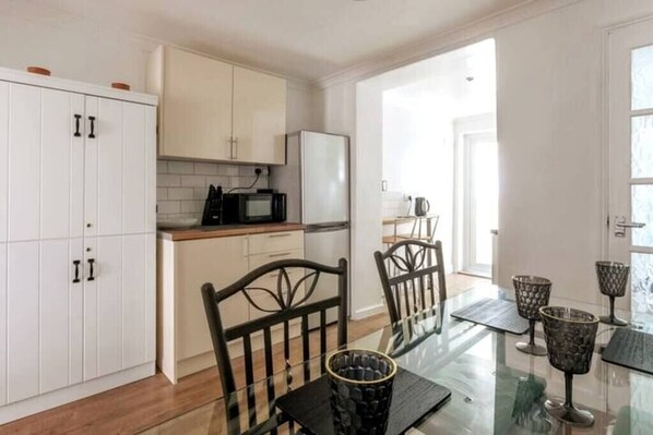 A modern kitchen with white cabinets, a microwave, and a refrigerator. There is a dining table with chairs and a glass top. - Stylish 2BD Family Hideaway in Dover (Dover)