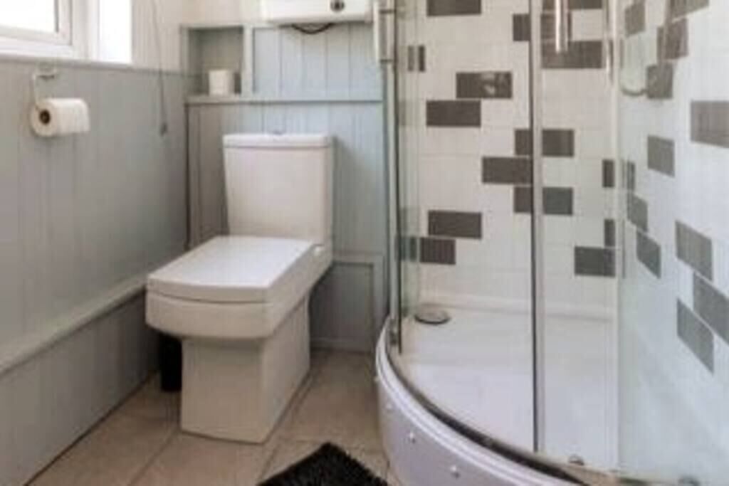 Et badeværelse med toilet, bruser med glasdøre og håndvask.