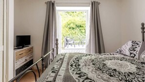 A bedroom with a bed, a TV on a dresser, and a view of a balcony with chairs. - Stylish 2BD Family Hideaway in Dover (Dover)