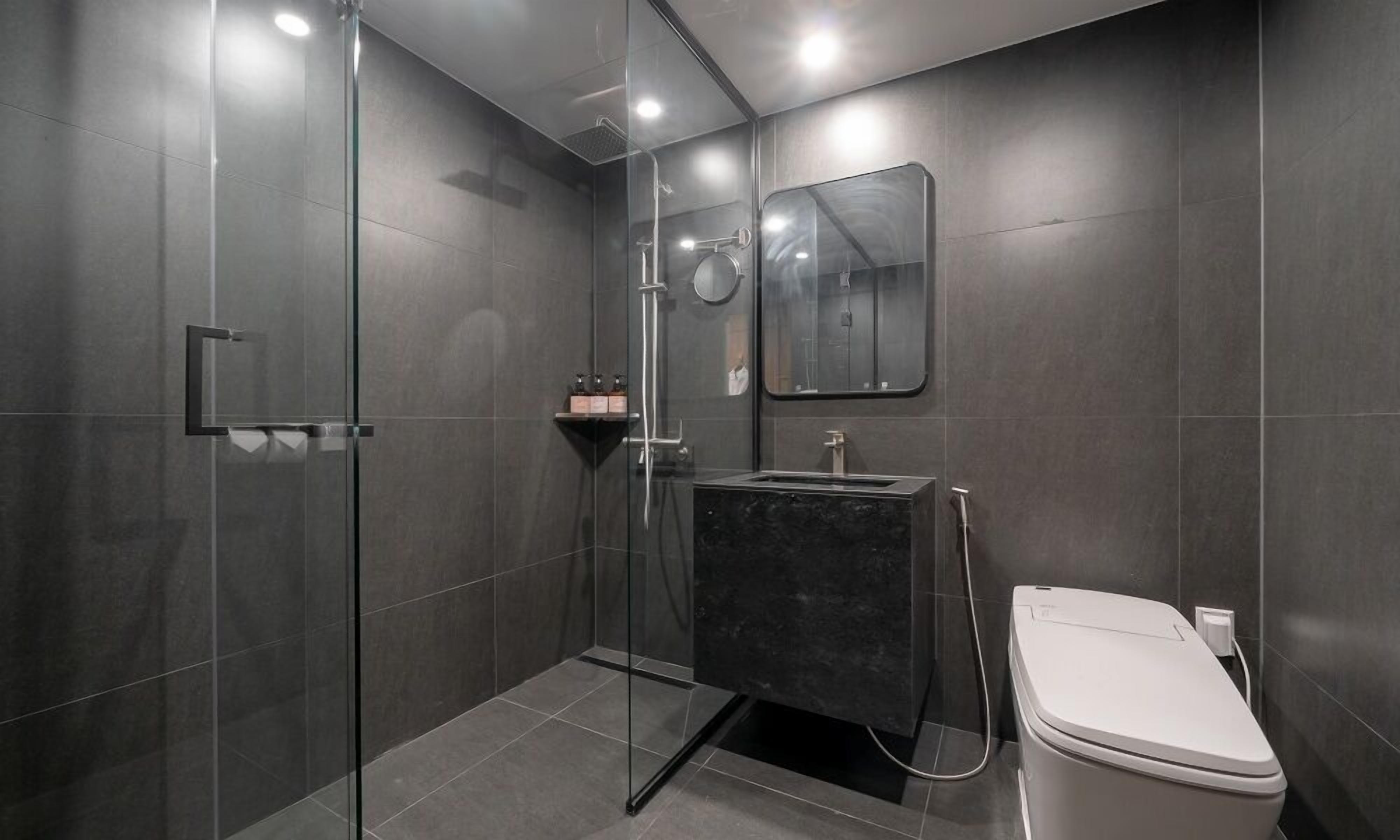 A modern bathroom with a glass shower enclosure, a black sink, and a white toilet.