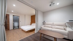 A modern hotel room with a wooden floor, a white bed, a beige sofa, and a small wooden table. - Simjak Hotel Dongtan By Anook (Hwaseong)