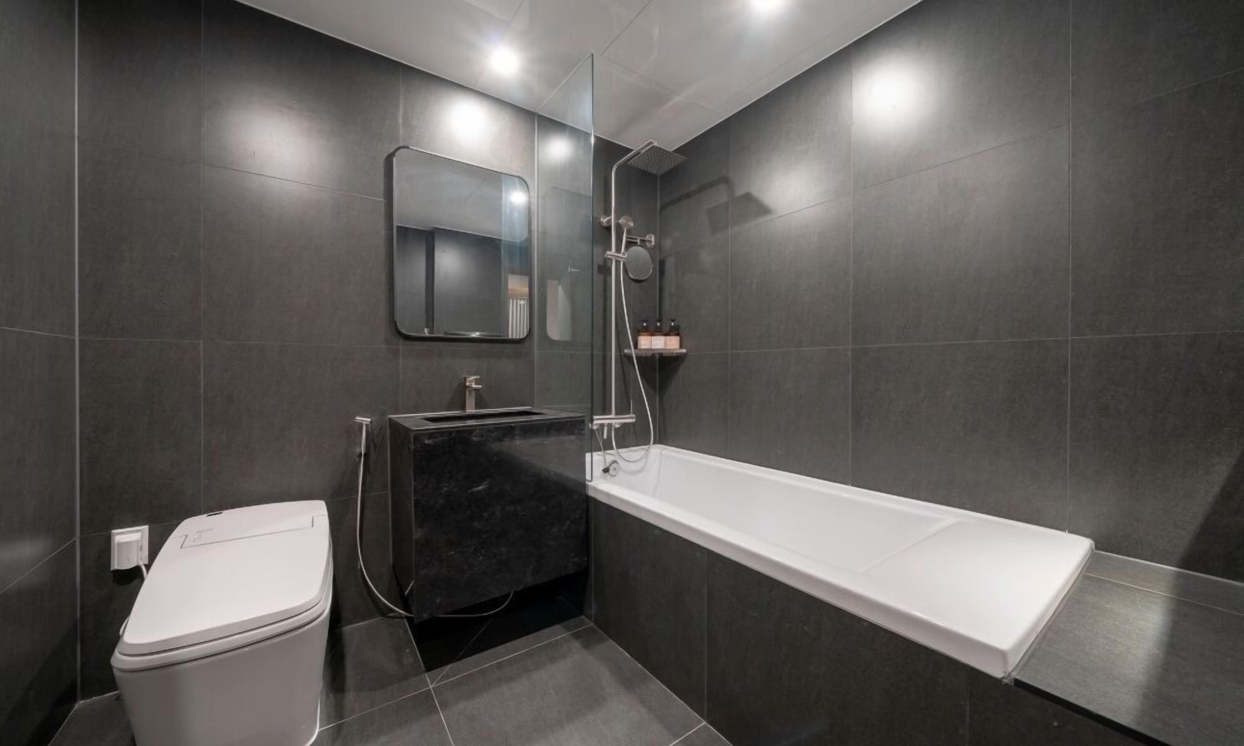 A modern bathroom with a toilet, a black sink, a large bathtub, and a glass shower enclosure.