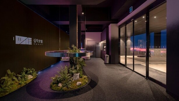 A modern interior with a reception desk, a small indoor garden, and a glass door leading outside. - Simjak Hotel Dongtan By Anook (Hwaseong)