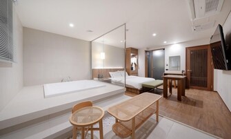 Una habitación de hotel moderna con una bañera grande, una cama, una mesita y un área de descanso con sillas de mimbre.