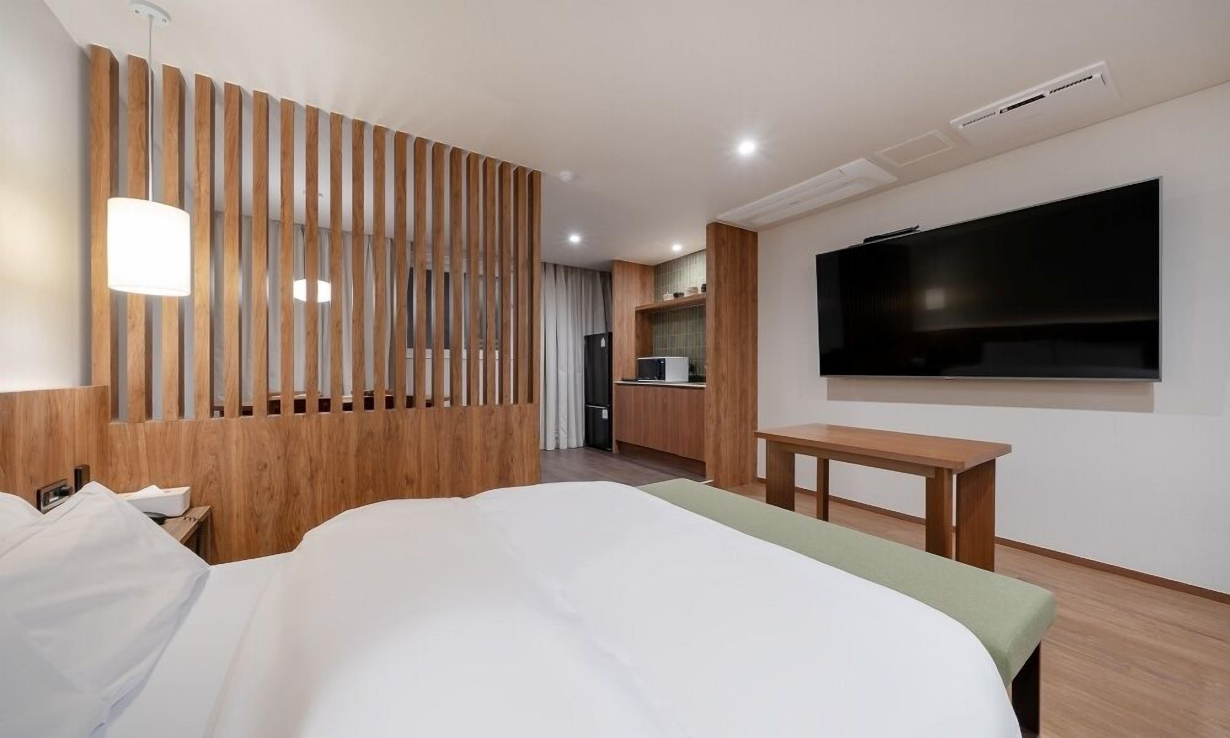 A hotel room with a bed, a TV, a desk, and a kitchenette.
