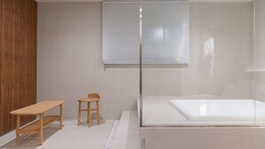 A modern bathroom with a glass shower enclosure, a wooden bench, and a small stool. - Simjak Hotel Dongtan By Anook (Hwaseong)