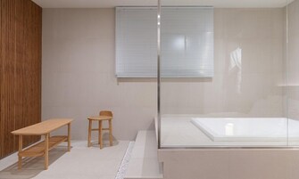 Un baño moderno con cabina de ducha de vidrio, un banco de madera y un taburete pequeño.